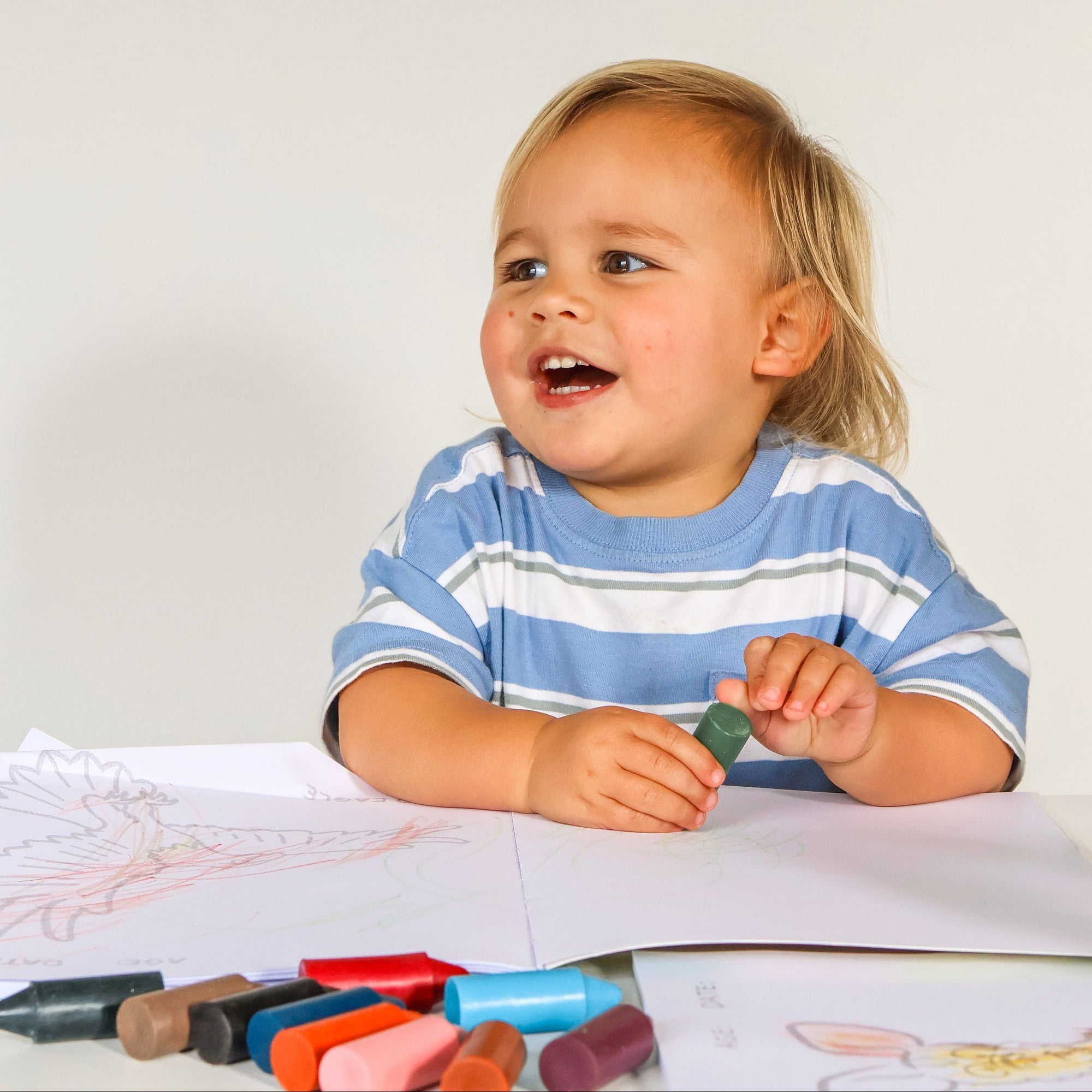 Child sitting at a table with drawing materials, smiling.
